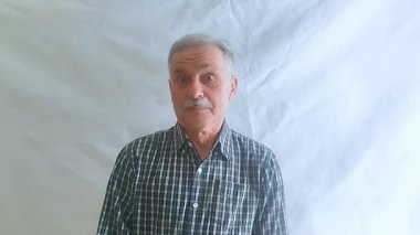 Bıyıklı ve kareli gömlekli yaşlı bir adam hayretle kameraya bakar. Beyaz arkaplanda bir portre.