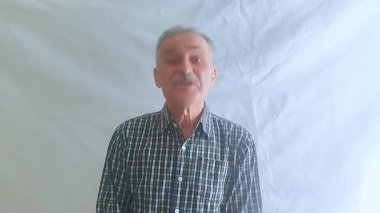 Hevesli bir ruh hali içinde yaşlı bir adam evet der, başını sallar ve kameraya bakar. Beyaz arkaplanda bir portre.