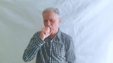 Kareli gömlekli yaşlı bir adam çok sert öksürüyor, midesi bulanıyor ve üşütüyor. Beyaz arkaplanda bir portre.