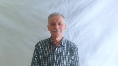 Bıyıklı ve kareli gömlekli yaşlı bir adam hayretle kameraya bakar. Beyaz arkaplanda bir portre.