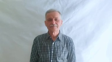 Hevesli bir ruh hali içinde yaşlı bir adam elini kibarca sallıyor ve kameraya bakıyor. Beyaz arkaplanda bir portre.