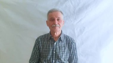 Hevesli bir ruh hali içinde yaşlı bir adam başparmağını kaldırır, başını olumlu bir şekilde sallar ve kameraya bakar. Beyaz arkaplanda bir portre.