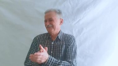 Kareli gömlekli yaşlı bir adam başarısız bir performansı alaycı bir şekilde alkışlıyor. Beyaz arkaplanda bir portre.