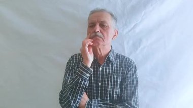 Kareli gömlekli yaşlı bir adam aktif olarak bir sorun düşünüyor ve doğru çözüm ona geliyor. Beyaz arkaplanda bir portre.