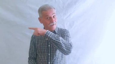 Kareli gömlekli yaşlı bir adam parmağını yana doğru gösteriyor ve bağlantıyı takip etmeyi öneriyor. Beyaz arkaplanda bir portre.