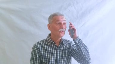 Kareli gömlekli yaşlı bir adam akıllı telefonuyla torunlarıyla konuşuyor. Beyaz arkaplanda bir portre.