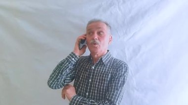 Kareli gömlekli yaşlı bir adam akıllı telefonuyla torunlarıyla konuşuyor. Beyaz arkaplanda bir portre.