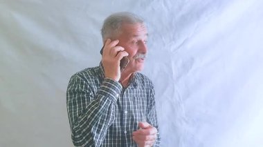 Kareli gömlekli yaşlı bir adam akıllı telefonuyla torunlarıyla konuşuyor. Beyaz arkaplanda bir portre.
