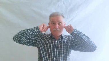 Kareli gömlekli yaşlı bir adam ellerini yüksek seslerden dolayı kulaklarıyla kapatır. Beyaz arkaplanda bir portre.
