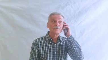 Kareli gömlekli yaşlı bir adam akıllı telefonuyla doktora danışıyor. Beyaz arkaplanda bir portre.