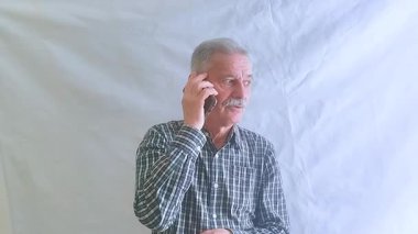 Kareli gömlekli yaşlı bir adam akıllı telefonuyla doktora danışıyor. Beyaz arkaplanda bir portre.