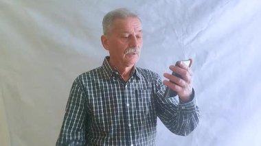 Kareli gömlekli yaşlı bir adam, akıllı telefonuyla haberlere bakıyor. Beyaz arkaplanda bir portre.
