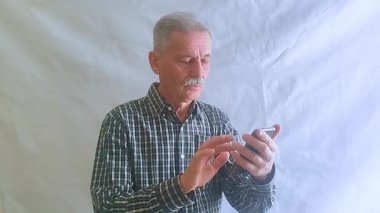 Kareli gömlekli yaşlı bir adam, akıllı telefonuyla haberlere bakıyor. Beyaz arkaplanda bir portre.