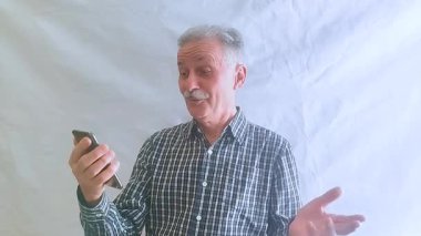 Kareli tişörtlü yaşlı bir adam torunlarıyla telefon görüşmesinde konuşuyor. Beyaz arkaplanda bir portre.