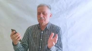 Kareli tişörtlü yaşlı bir adam torunlarıyla telefon görüşmesinde konuşuyor. Beyaz arkaplanda bir portre.