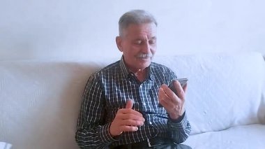 Kareli tişörtlü yaşlı bir adam torunlarıyla telefon görüşmesinde konuşuyor. Beyaz arkaplanda bir portre.