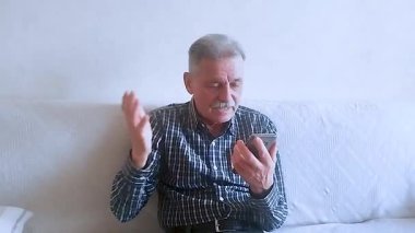 Kareli tişörtlü yaşlı bir adam torunlarıyla telefon görüşmesinde konuşuyor. Beyaz arkaplanda bir portre.