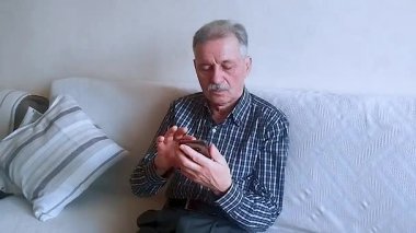 Kareli gömlekli yaşlı bir adam, akıllı telefonuyla haberlere bakıyor. Beyaz arkaplanda bir portre.