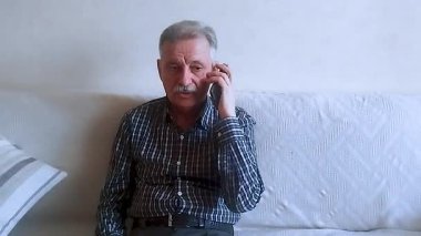 Kareli gömlekli yaşlı bir adam akıllı telefonuyla doktora danışıyor. Beyaz arkaplanda bir portre.