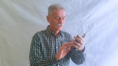 Kareli gömlekli yaşlı bir adam, akıllı telefonuyla haberlere bakıyor. Beyaz arkaplanda bir portre.