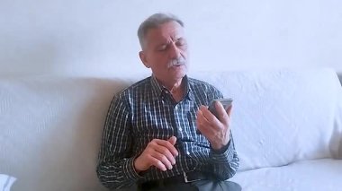 Kareli tişörtlü yaşlı bir adam torunlarıyla telefon görüşmesinde konuşuyor. Beyaz arkaplanda bir portre.