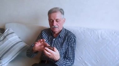 Kareli gömlekli yaşlı bir adam, akıllı telefonuyla haberlere bakıyor. Beyaz arkaplanda bir portre.