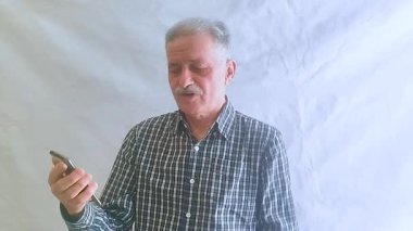 Kareli tişörtlü yaşlı bir adam torunlarıyla telefon görüşmesinde konuşuyor. Beyaz arkaplanda bir portre.