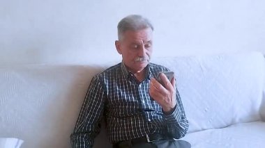 Kareli gömlekli yaşlı bir adam akıllı telefonuyla doktora danışıyor. Beyaz arkaplanda bir portre.