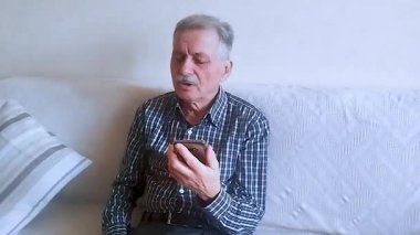 Kareli gömlekli yaşlı bir adam akıllı telefonuyla doktora danışıyor. Beyaz arkaplanda bir portre.