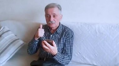 Kareli gömlekli yaşlı bir adam akıllı telefonuyla doktora danışıyor. Beyaz arkaplanda bir portre.