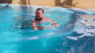 Genç bir adam temiz suda yüzerek havuzun kenarına tutunuyor. Yüksek kalite 4k görüntü