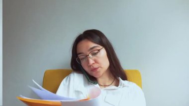 Genç ve çekici bir iş kadını telefonda konuşur ve belgelere bakar. Yüksek kaliteli FullHD görüntüler