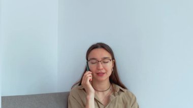 Genç ve çekici bir kız oturma odasında otururken cep telefonuyla konuşuyor. Yüksek kalite 4k görüntü