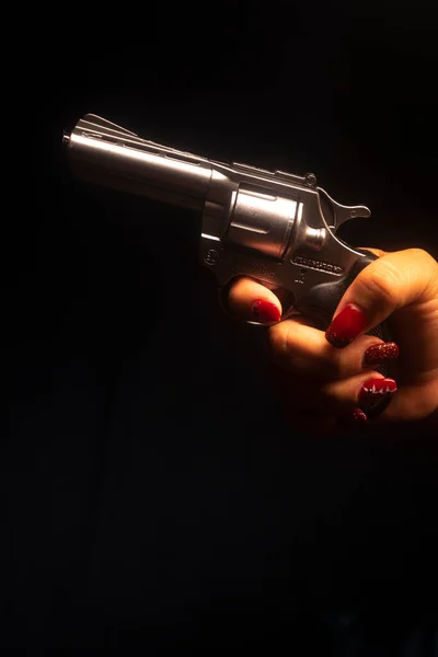 Lady spy detective  with painted red nail varnish holding pistol gun at night