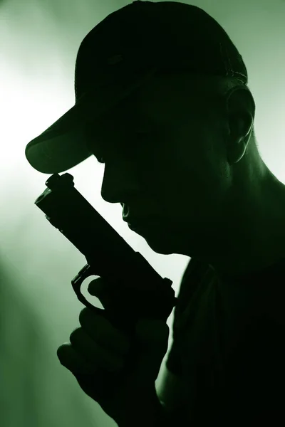 Young criminal killer in cap with gun pistol in dark silhouette photo book cover thriller design.