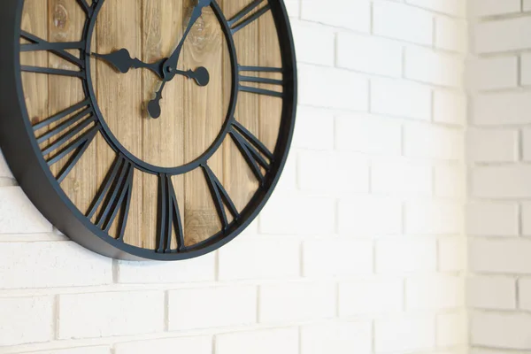 Wooden clock with black hands and numbers placed on white wallpaper with brick design