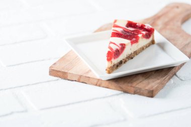 Ahududu kıvrımlı cheesecake dilimi kare tabakta beyaz tuğla masa