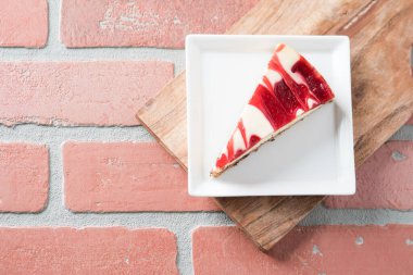 Ahududu kıvrımlı cheesecake dilimi kare tabakta kırmızı tuğla masa