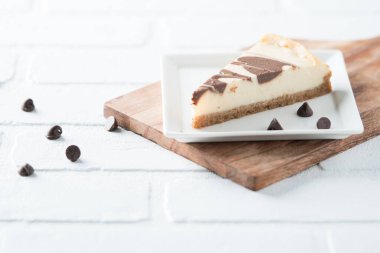 Çikolata kıvrımlı cheesecake dilimi kare tabakta beyaz tuğlada