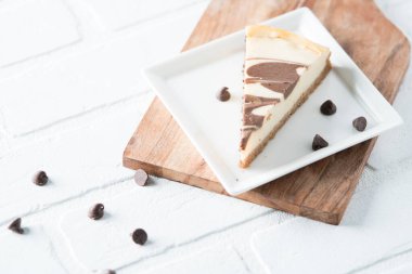 Çikolata kıvrımlı cheesecake dilimi kare tabakta beyaz tuğlada