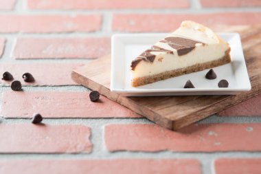 Çikolata kıvrımlı cheesecake dilimi kare tabakta kırmızı tuğlada