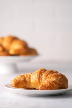 Beyaz tabakta gevrek gevrek kruvasan rulosu ve sıkıntılı bir masa.