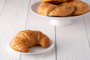 Beyaz tabakta gevrek gevrek kruvasan rulosu ve sıkıntılı bir masa.