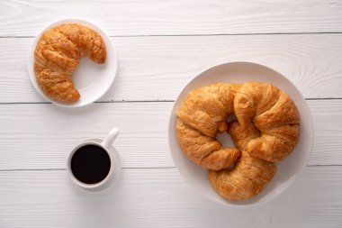 Beyaz tabakta gevrek gevrek kruvasan rulosu ve sıkıntılı bir masa.