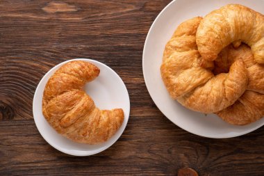 Beyaz tabakta gevrek gevrek kruvasan rulosu ve sıkıntılı bir masa.