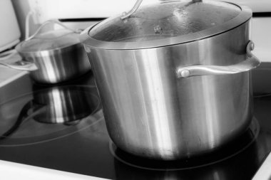 Evcil bir mutfakta seramik bir ocağın üstünde paslanmaz çelik tencereler..