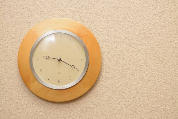 A wood clock mounted on a textured wall. Tme is 9:20