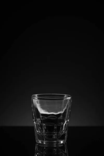 Stacked clear glass shot glasses black background reflective surface