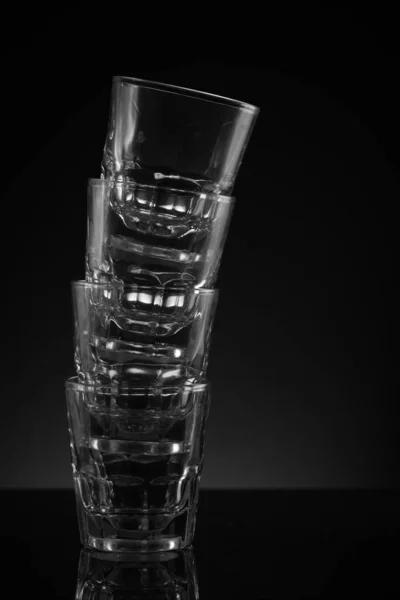 Stacked clear glass shot glasses black background reflective surface and awkward arrangement