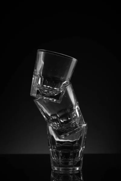 Stacked clear glass shot glasses black background reflective surface and awkward arrangement